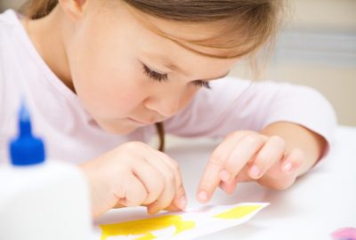 Little girl doing arts and crafts in preschool Cute little girl applying a color paper using glue while doing arts and crafts in preschool